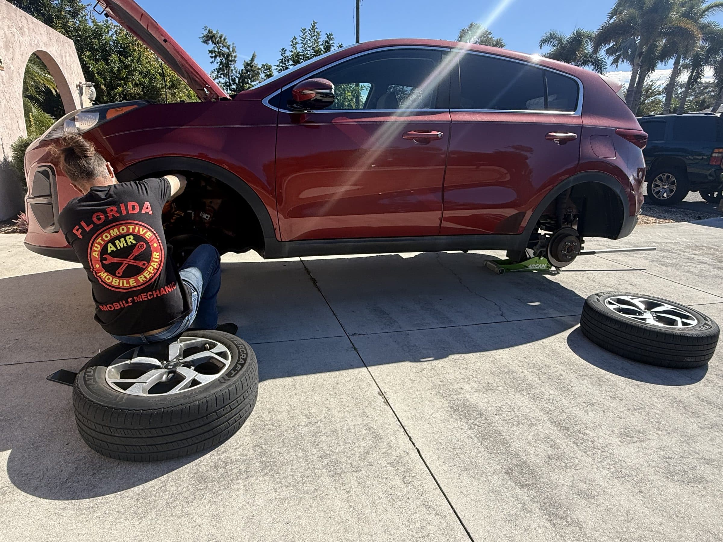 AMR mobile mechanic in a branded shirt replacing brakes on an SUV in a customer's Florida driveway
